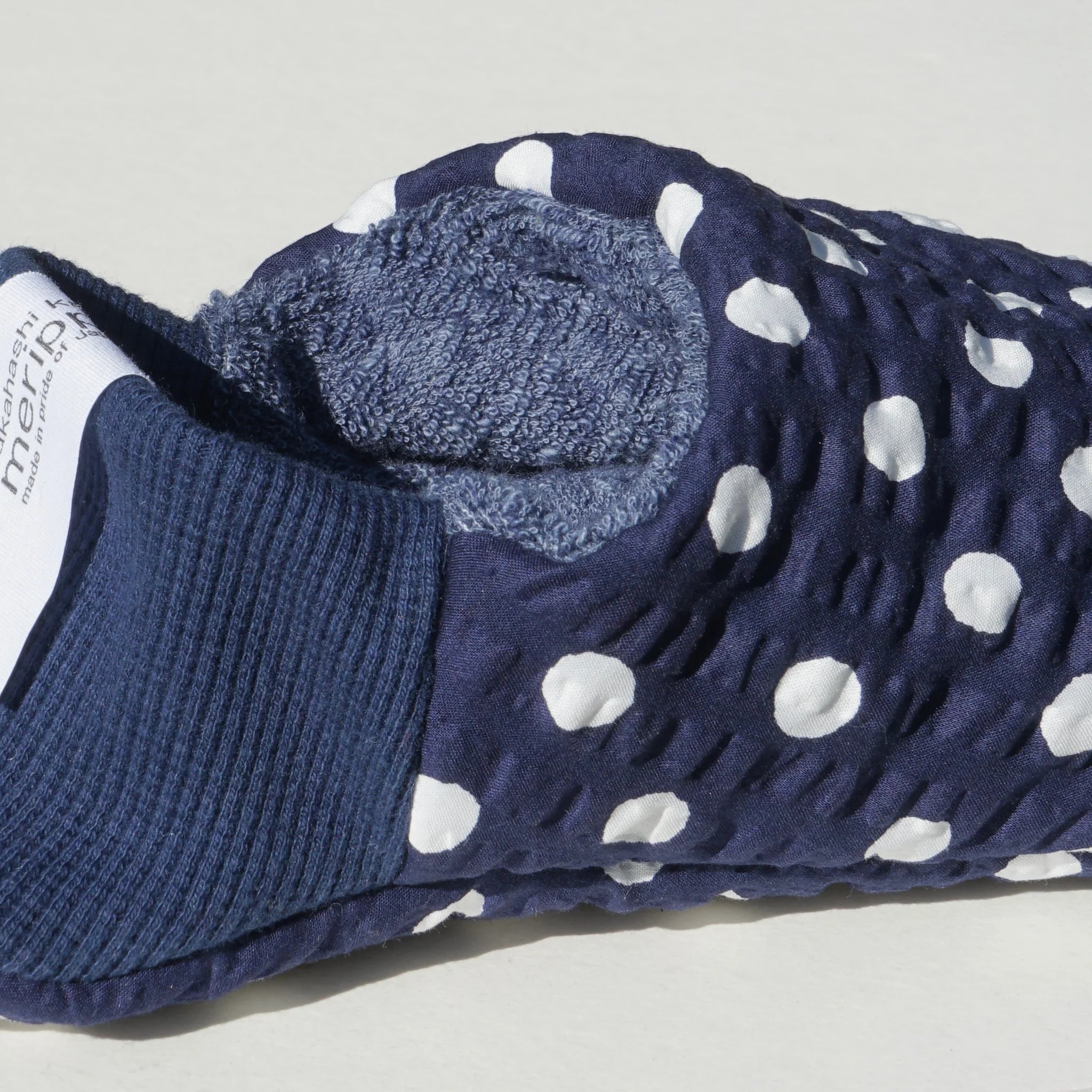 Close up of navy blue and white polka dot slippers with blue interior and blue heels on a white background